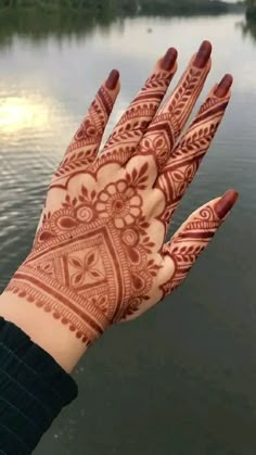 a woman's hand with henna tattoos on it, next to the water