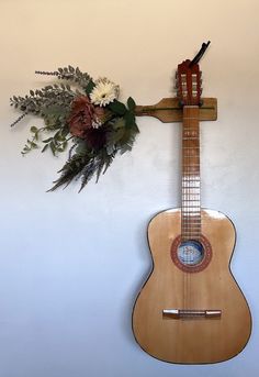 a wooden guitar hanging on the wall with flowers and a cross in front of it