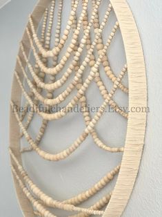 a wall hanging made out of white wood beads and rope with an intricate design on it