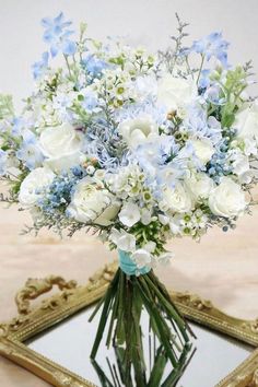 a bouquet of white and blue flowers sitting in front of a mirror on a table