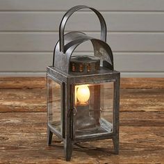 an old fashioned metal lantern with a light on it's side sitting on a wooden table