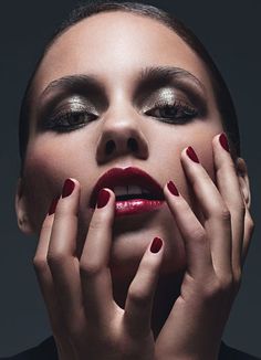 a woman with red and silver makeup holding her hands to her face