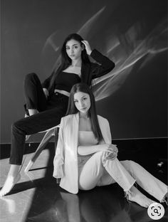 two women sitting on the floor in front of a black and white background, one with long hair