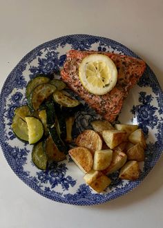 a blue and white plate topped with meat, potatoes and vegetables next to a slice of lemon