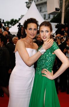 two women standing next to each other on a red carpet with cameras in the background