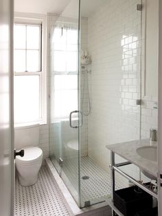 a white tiled bathroom with a walk in shower next to a toilet and sink area