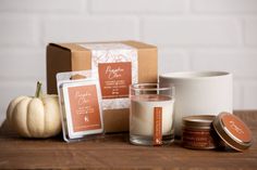 an assortment of candles on a table next to a box and candle holder with pumpkins