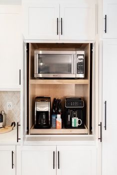 a kitchen with white cupboards and appliances inside of it's door open to reveal a coffee maker, toaster, and other items on the countertop