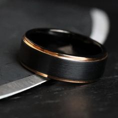 a black and gold wedding band sitting next to a knife