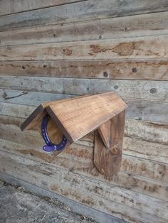 a wooden bird house with a purple object on it's back end in front of a wood paneled wall