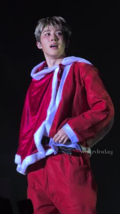 a man dressed as santa clause standing in front of a black background with his hands on his hips