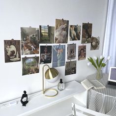 a white desk topped with a laptop computer next to a wall covered in pictures and photos