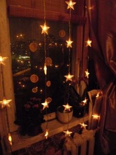 a window with stars hanging from it's side in front of a curtained window sill