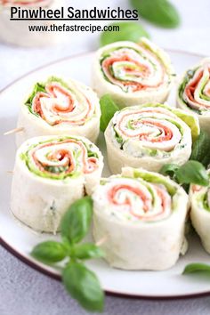 there are many rolls on the plate with green leafy garnishes around them