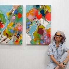 an older woman sitting in front of two colorful paintings on the wall with her legs crossed