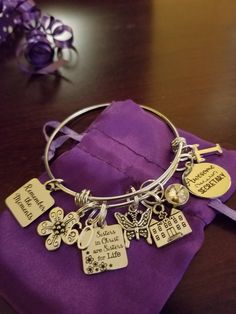 a close up of a bracelet on a table with purple cloth and flowers in the background