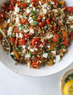 a white bowl filled with grains, tomatoes and feta cheese