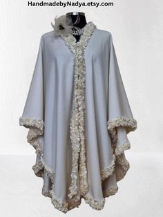 Experience the ultimate luxurious with this handcrafted Embellished Cashmere cape, poncho. Delicately designed with intricate soutache and pearl handwork trim, this shawl is a testament to the skill and craftsmanship of the artisan. The bordered trim adds an original touch, elevating the cape's beauty to a whole new level. This one-of-a-kind piece is perfect for those who appreciate the finer things in life and desire a unique statement accessory. Stay cozy and stylish this winter with this truly exquisite cape. Elegant White Capelet With Cape Sleeves, Elegant Winter Capelet With Cape Sleeves, Elegant Beige Cape Poncho, Elegant Beige Poncho, Elegant Winter Capelet, Elegant White Poncho For Winter, Elegant White Cape With Cape Sleeves, Elegant White Winter Poncho, Elegant Winter Cape Poncho