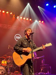 a man standing in front of a microphone while holding a guitar