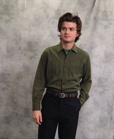 a young man is standing in front of a gray backdrop wearing a green shirt and black pants