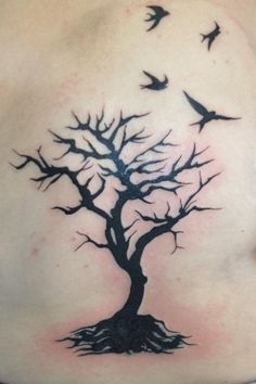 a woman's back with a tree and birds tattoo on her shoulder, which is decorated in black ink