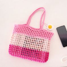 a pink and white crocheted bag next to a cell phone on a table