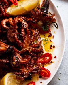 an octopus dish on a white plate with lemon wedges and red peppers next to it