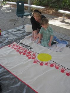 a woman and child are painting on a large white sheet with red flowers in the center