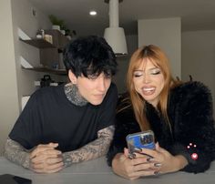 a man and woman sitting at a table looking at a cell phone with tattoos on their arms