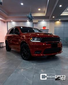 a red dodge suv is parked in a showroom with lights on and black rims