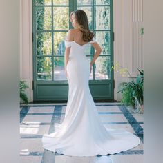 a woman standing in front of a green door wearing a white wedding dress with off the shoulder sleeves