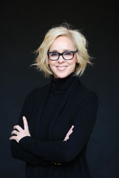 a woman with glasses is smiling and posing for the camera in front of a black background