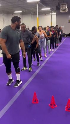 a group of people standing around cones on top of a purple floor in a gym