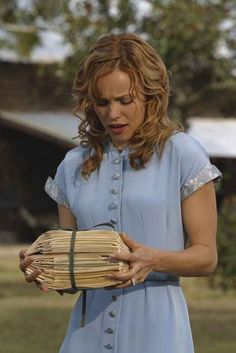 a woman in a blue dress holding a stack of books and looking down at it