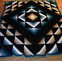 a crocheted blanket is on the floor in front of a wooden table top