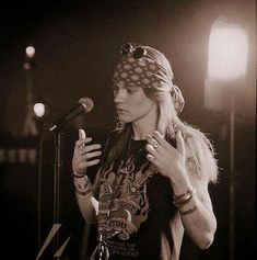 a woman standing in front of a microphone with her hand on her hip and wearing bandana