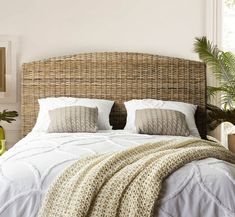 a bed with pillows and blankets on top of it in a bedroom next to a potted plant