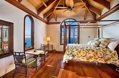 a bedroom with wood flooring and ceiling fan in it's center window overlooking the ocean