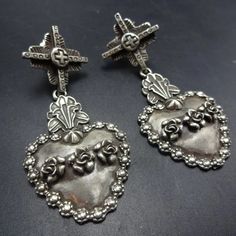 GREGORY SEGURA SOUTHWEST SANTA FE ARTISAN STERLING SILVER EARRINGS DESCRIPTION:  Solid sterling silver hearts adorned and framed with flowers hang from Tesuque crosses. These magnificent earrings by celebrated Santa Fe silversmith Gregory Segura will be a cherished addition to your collection of quality Southwestern and Native American jewelry. MEASUREMENTS: Earrings measure 2 3/8" x 1" WEIGHT: 24.2 grams SIGNED:  Gregory Segura  STERLING:  yes, stamped STERLING Traditional Silver Heart Earrings, Basket Earrings, Cowboy Jewelry, Silver Cross Earrings, Jewelry Measurements, Mexican Silver Jewelry, Dope Jewelry, Funky Jewelry, Denver Co