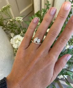 a woman's hand with a ring on it and flowers in the back ground