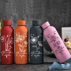 three different colored water bottles sitting next to each other on a table with flowers in the background