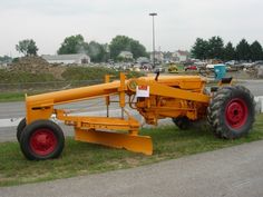 an orange tractor sitting in the grass next to a road and some cars behind it