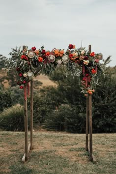 an arch decorated with flowers and greenery stands in the middle of a grassy field