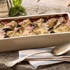 a casserole dish on a wooden table with spoons and utensils