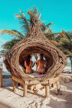 two women in bikinis sitting on a wooden structure at the beach with palm trees