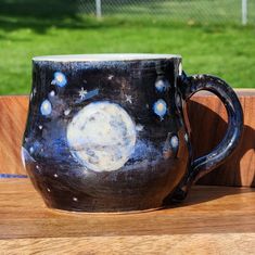 a black and white coffee cup sitting on top of a wooden table next to a fence