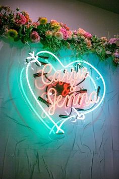 a neon sign that says caring for spring on the side of a wall with flowers