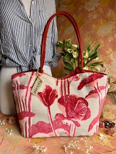 a woman is holding a red and white purse with flowers on the front, while wearing a striped shirt