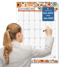 a woman writing on a calendar board with autumn decorations around her and an orange background