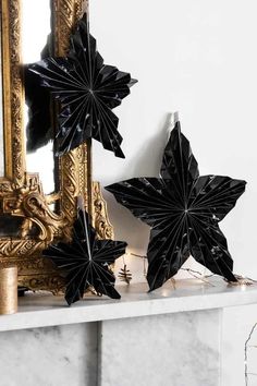 two black paper stars sitting on top of a mantle next to a mirror and candle